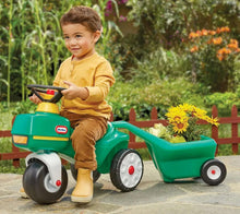 Green ride-on tractor with yellow seat and attached cart; toddler sitting and holding wheel