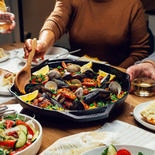 Round cast iron skillet with handles, filled with seafood and vegetables