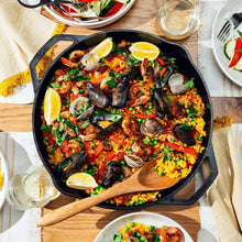 Round cast iron skillet filled with paella-style rice, clams, and vegetables