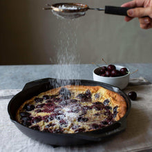 Cast iron skillet with handle, dusted pastry on top, grapes nearby