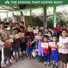 Children holding coffee bags under a school shelter with large green roof