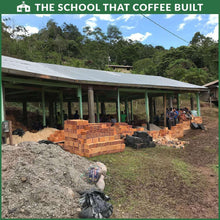 School building under construction with stacked materials and The School That Coffee Built logo