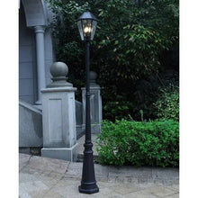 Black solar post light on a walkway, with lantern glow between garden shrubs