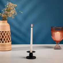 Black candle holder with lit white pillar candle on round base