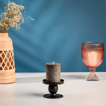 Black candle holder with gray pillar candle and lit wick