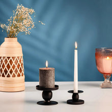Black candle holder with tall lit white pillar candle