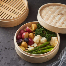 Bamboo steamer basket lid open with vegetables inside, beige