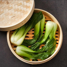 Bamboo steamer basket with woven lid, filled with bok choy and greens