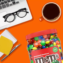 Peanut butter M&M's candy jar with red lid and colorful candy pieces on desk