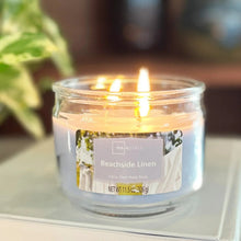 Lit blue glass jar candle with Beachside Linen label, 11.5 oz, three wicks