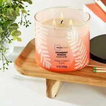 Cranberry-mimosa scented candle jar with three flames, black lid, on wooden stand