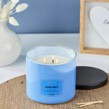 Blue scented candle jar with three wicks burning in glass rim