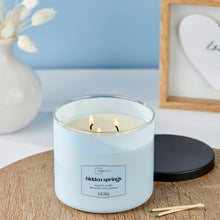 Blue 3-wick candle jar with black lid, lit flames visible through clear rim