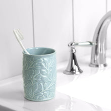 Light blue ceramic toothbrush holder with embossed leaf pattern; holds a toothbrush.