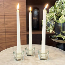 Three ivory taper candles burning in clear holders