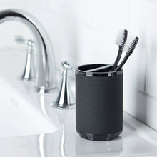 Black ribbed plastic toothbrush holder cup with toothbrushes inside
