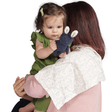 Plush bunny rattle in baby hands, attached to light patterned cloth