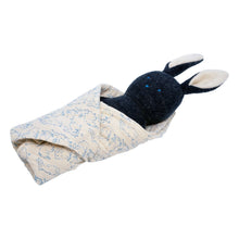 Plush bunny rattle with embroidered eyes tucked in light patterned burp cloth