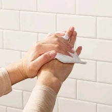 Centerpull paper towel being pulled from dispenser, held by hands at bathroom wall