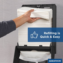 Black folded paper towel dispenser open for refilling with stacked towels inside