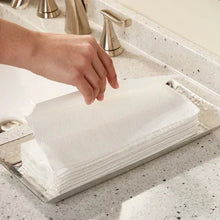 Hand lifting a white 2-ply C-fold paper towel from a stack