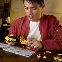 Person assembling a yellow car brick model from small parts on an instruction sheet