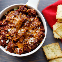Bowl of chili with melted cheese and diced onions, served with crackers