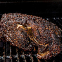 Grilled pork shoulder coated in dark spice rub on barbecue grate.