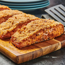 Sliced meat pieces coated in orange-brown spice rub on wooden cutting board.