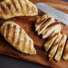 Sliced grilled chicken breast on a wooden board, with seasoning specks