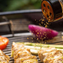 Grill seasoning shaker over chicken on a barbecue grill, with vegetables nearby