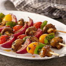 Grilled meat skewers on a plate with sliced peppers and mushrooms