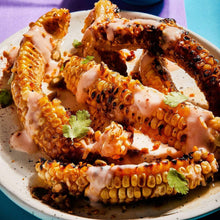 Grilled corn pieces with creamy topping, spice dust, and cilantro garnish on a plate