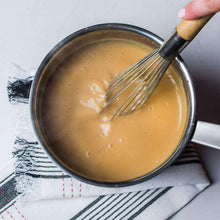 Poultry seasoning mixed into beige sauce in saucepan with whisk