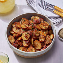 Seasoned sliced potatoes in a gray bowl with herbs