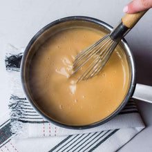 Saucepan of smooth poultry gravy being whisked with a wooden-handled whisk