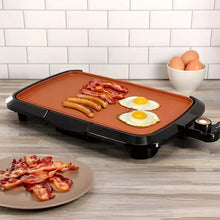 Electric grill with copper-toned plate holding bacon strips and two sunny-side eggs