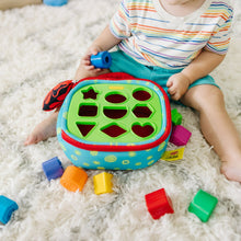 Baby playing with Take-Along shape sorter on rug with green hole panel and blocks