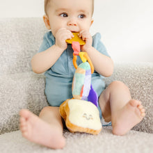 Baby holding soft clip-on sensory toy with bread slice face and multicolor fabric straps