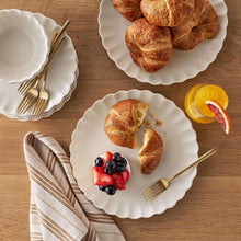 Cream scalloped dinnerware set with plates and bowls, styled for serving bread and fruit
