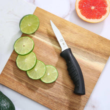Paring knife with black handle on a wooden board with lime slices
