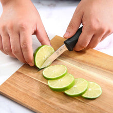Paring knife with black handle slicing lime on a wooden cutting board