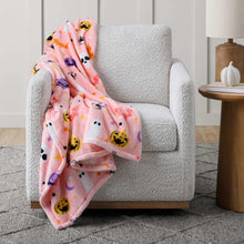 Pink Halloween pumpkin and ghost lounge throw blanket draped over a light gray armchair