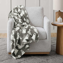 Gray and white Halloween ghost lounge throw blanket draped over a light gray armchair