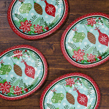 Multiple oval holiday paper plates with red border and ornament pattern on wood surface