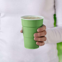 Green disposable plastic cup held in a hand with clear liquid inside