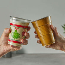 Holiday cups held in hands, one green ornament cup and one gold metallic cup