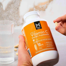 Hand holding Vitamin C dietary supplement bottle with orange label and white cap