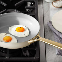 Cream ceramic frying pan with gold handle, cooking two sunny-side-up eggs