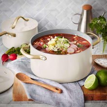 Cream ceramic soup pot with gold handles, holding red soup with toppings